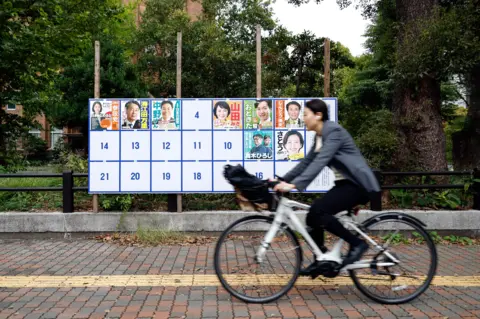 EPA-EFE/REX/Shutterstock A cyclist passes a board displaying campaign posters of candidates running for the upcoming general elections in Tokyo, Japan.