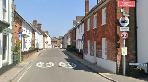 Google A narrow lane lined with terraced houses. On either side of the road is a 20mph speed limit sign and two white 20 signs are painted on the tarmac.