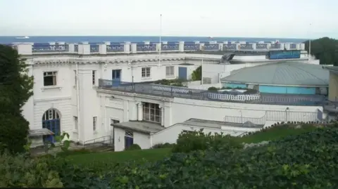 Top shot of large white Edwardian building cut in the cliffs with sea behind 