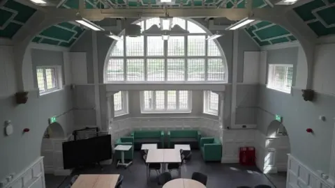 The room in Ysgol Gymraeg Y Trallwng is tall and symmetrical, with a high vaulted ceiling and a large arched window dominating the far wall.