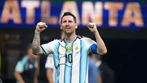 Getty Images Lionel Messi with both his arms up celebrating. He is wearing a blue and white Argentina shirt with the number 10 in the middle and he is smiling.