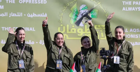 Reuters Naama Levy, Liri Albag, Daniella Gilboa and Karina Ariev wearing khaki clothes, stand on a stage and wave to a crowd.