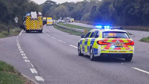 A police car is parked on an motorway with fire engines further down the road