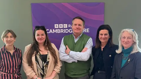 5 people stand in front of a sign which says BBC Radio Cambridgeshire