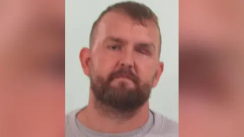 Image of Steve. He has a blonde/ginger beard and large ears. He is wearing a grey jumper.