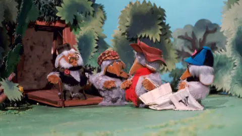 The Cookie Jar Company A scene taken from The Wombles' TV show where four Wombles are seen interacting outside. 