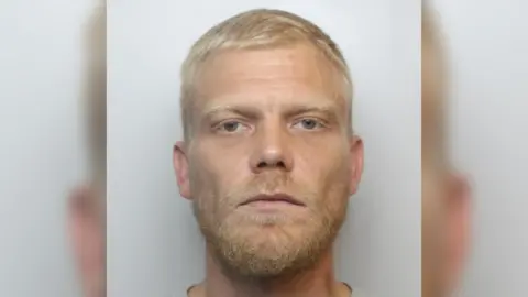 A mugshot of Craig Coney, he has blonde hair and beard and blue eyes