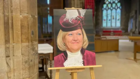 Simon Thake A blonde woman with smart velvet purple jacket and matching hat