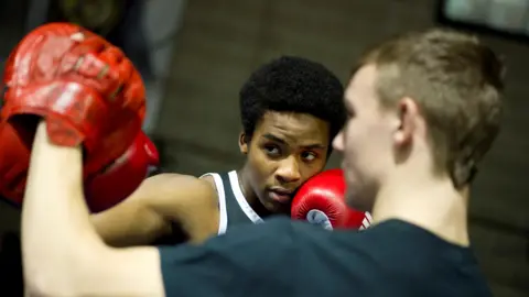 Dennis Stinchcombe Boys boxing in a ring wearing red gloves