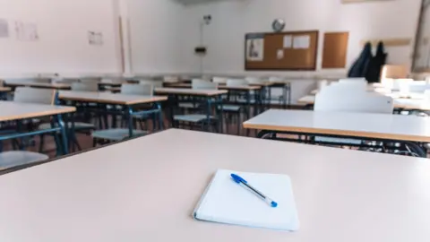 Getty Images An empty classroom, with desks and chairs, and a pad of paper and a pen on the closest table to the camera 