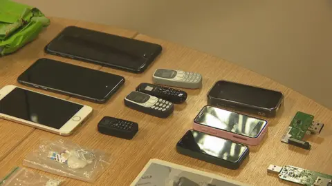On a rtable, we see a line of three iPhones, four smaller call-only phones, three older iPhone models and several home-made dongles. There is also a small plastic bag full of sim cards - all of which were in the drone's package.