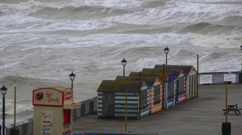 BBC Weather Watchers / Peter and Leah Beach huts on Hastings seafront during Storm Bert, grey, choppy sea seen in the background