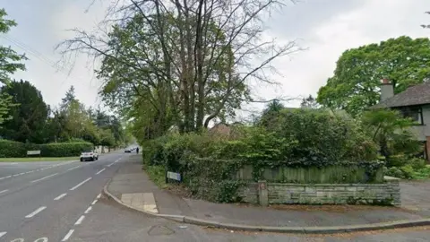 A Google street view of a main road, with roads on each side branching off into residential areas lined by fences.
