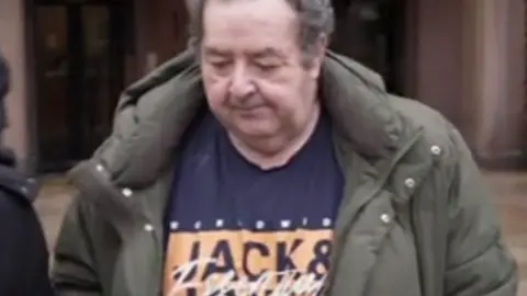 Gerard Woodhouse, who is middle-aged with thinning grey hair, is seen leaving Liverpool Magistrates' Court in December. He is wearing a blue t-shirt with a brand logo on it, and an olive green puffer-style jacket 