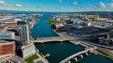 Aerial photo of Belfast City Skyline Cityscape Northern Ireland. The M3 bridge over the River Lagan, the Harland and Wolff cranes and the SSE Arena can all be seen in the shot.