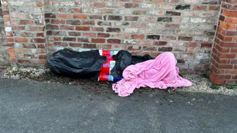 York BID Great Britain Nutcracker wrapped up in plastic bags and a pink blanket by a brick wall.