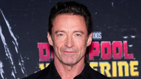 Getty Images Headshot of Hugh Jackman. He has dark hair and wear a black suit jacket