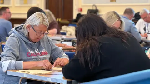 People sit at a table counting votes cast during the 2026 Jersey general election.