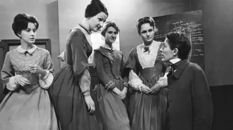 A black and white photo of Penelope Keith (second from left) appearing in a production of Pioneers of Social Change in 1962. The cast is in period Victorian dress