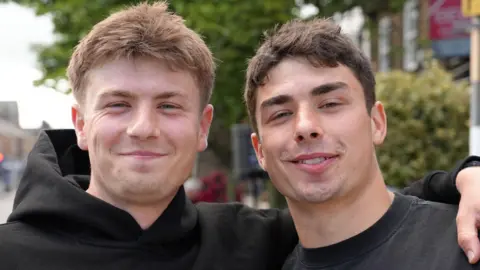 Borthers Euan and Andrew. Euan is clean shaven with short fair hair and has his arm around his broehr, who is clean shaven with short dark hair.