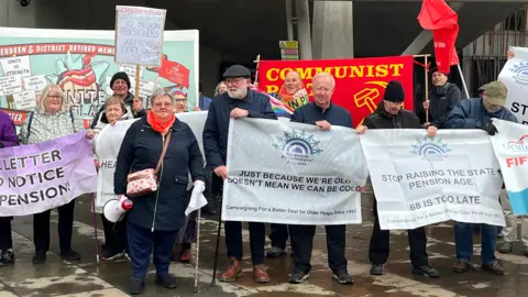 A number of people of pension age standing with banners and a megaphone outside the Scottish Parliament