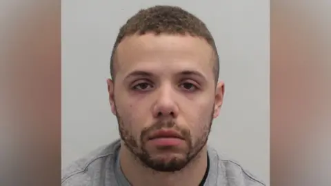 Met Police Mugshot of a man with a beard and short hair wearing a grey jumper