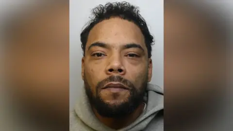 Photo of Jamie Ivers' prison mug shot. He is looking directly into the camera. The headshot photo includes a small portion of his grey hoodie. Jamie has black hair and a beard. 