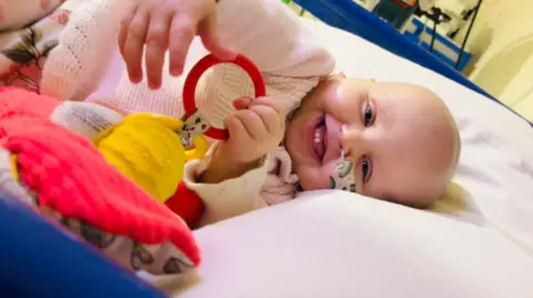 Family handout Melody is smiling at the camera in a hospital crib with a tube coming out her nose.