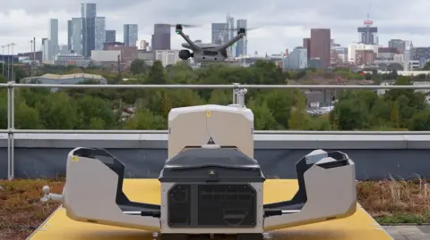 A drone hovering above an open docking box, with the Manchester skyline in the background.