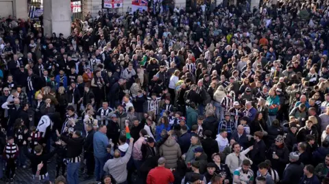 Owen Humphries/PA Wire Overhead view of a gathering of Newcastle United supporters. The crowd consisting of many hundreds of people, some wearing Newcastle United football strips. Many have their heads thrown back and seem to be celebrating or chanting. 