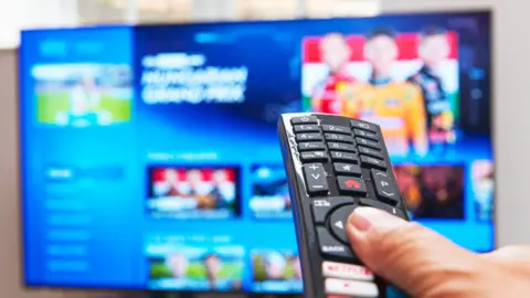 Close up of a person holding a TV remote, pointing at a smart TV