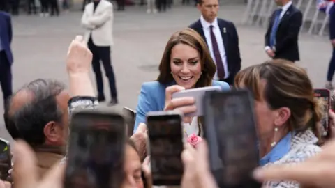 PA Media Mobile phones are held in the air to take a picture of the Princess of Wales as she smiles greeting crowds, dressed in a pale blue blazer