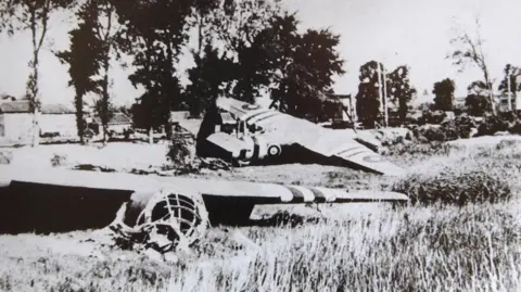 PA Archives/PA Images A black and white image of two broken gliders in a grassy field next to a river with a bank of trees alongside 