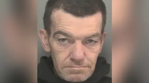 Undated handout custody photo issued by Merseyside Police of Steven Wales. He has dark brown hair and grey stubble.