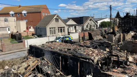 Stuart Woodward/BBC A row of destroyed houses in Jaywick with a police car in the background