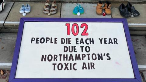 White banner with black writing saying that 102 people die from Northampton's toxic air