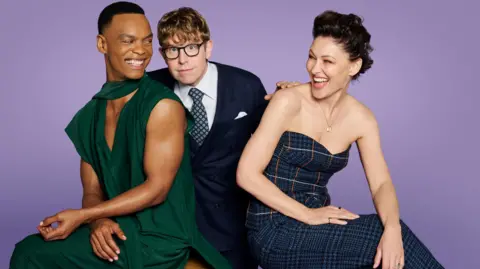 Josh Widdicombe, Emma Willis and Johannes Radebe holding glitter balls against a purple background