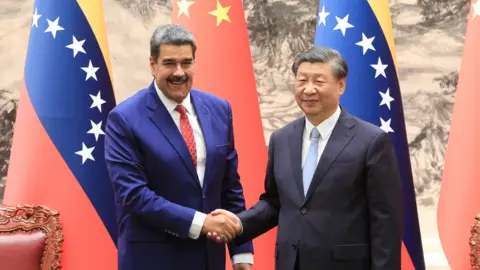 Venezuelan president Nicolás Maduro (L) and Chinese president Xi Jinping shake hands and smile in front of Venezuelan and Chinese flags at the palace in Beijing in 2023.