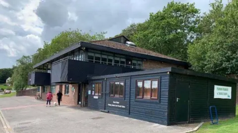 Bewl Events and Waterparks Ltd Two people walking their dog outside a bistro, which is located on a park. There are trees behind the building. 