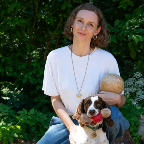BBC/Chris Waring Kim Errington, with a small dog, holds a wooden ball