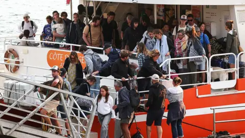 A number of passengers disembark from a boat