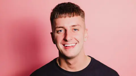 DAIRE pictured smiling in black tshirt with a pink background