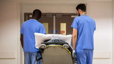 Medical staff accompany a patient on a trolley through a corridor inside the Royal London Hospital, part of the Barts Health NHS Trust, in London, U.K., on Thursday, Jan. 11, 2018. 