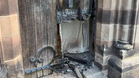 Shropshire Fire and Rescue Service A fire damaged wooden door in a stone wall with some of the wood turned to ash and a big hole in the bottom of it