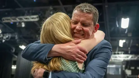 Matthew Horwood/Getty Images Rhun ap Iorwerth embracing a woman, smiling. He is wearing a blue suit and she is wearing a green top.