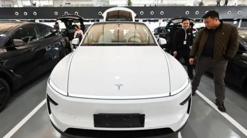 AFP via Getty Images People looking at a white Tesla car in a showroom in Beijing