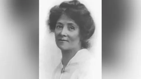 A black and white portrait picture of a woman with dark bushy hair and wearing a white top.