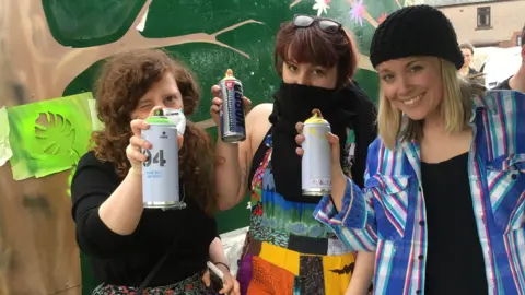 Creative Futures Three woman, two with their faces covered, carrying spray paint cans