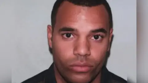 A close-up head-and-shoulders image of a Emem Udaw looking directly at the camera, with short dark hair with a plain light-coloured background.