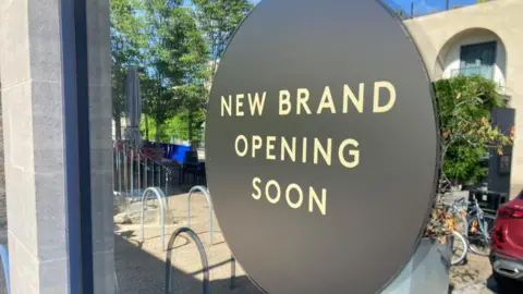 A sign in a window saying "New Brand Opening Soon"